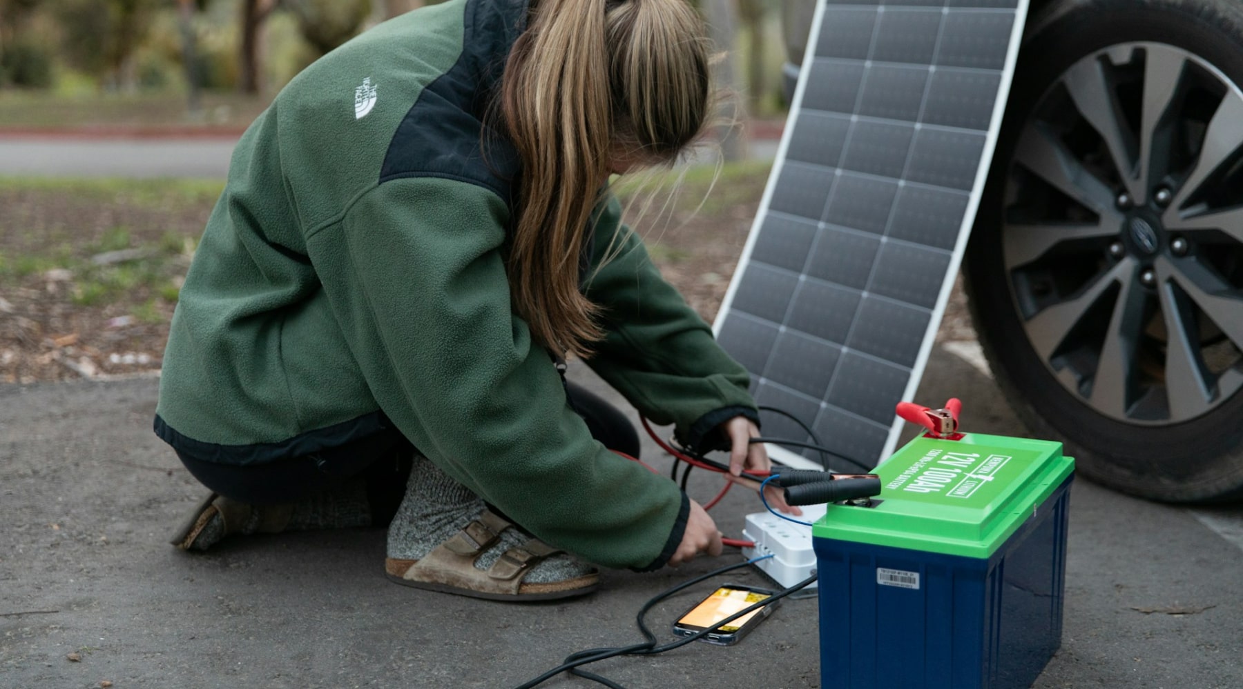 A picture showing a lady outdoors charging a solar panel via a battery