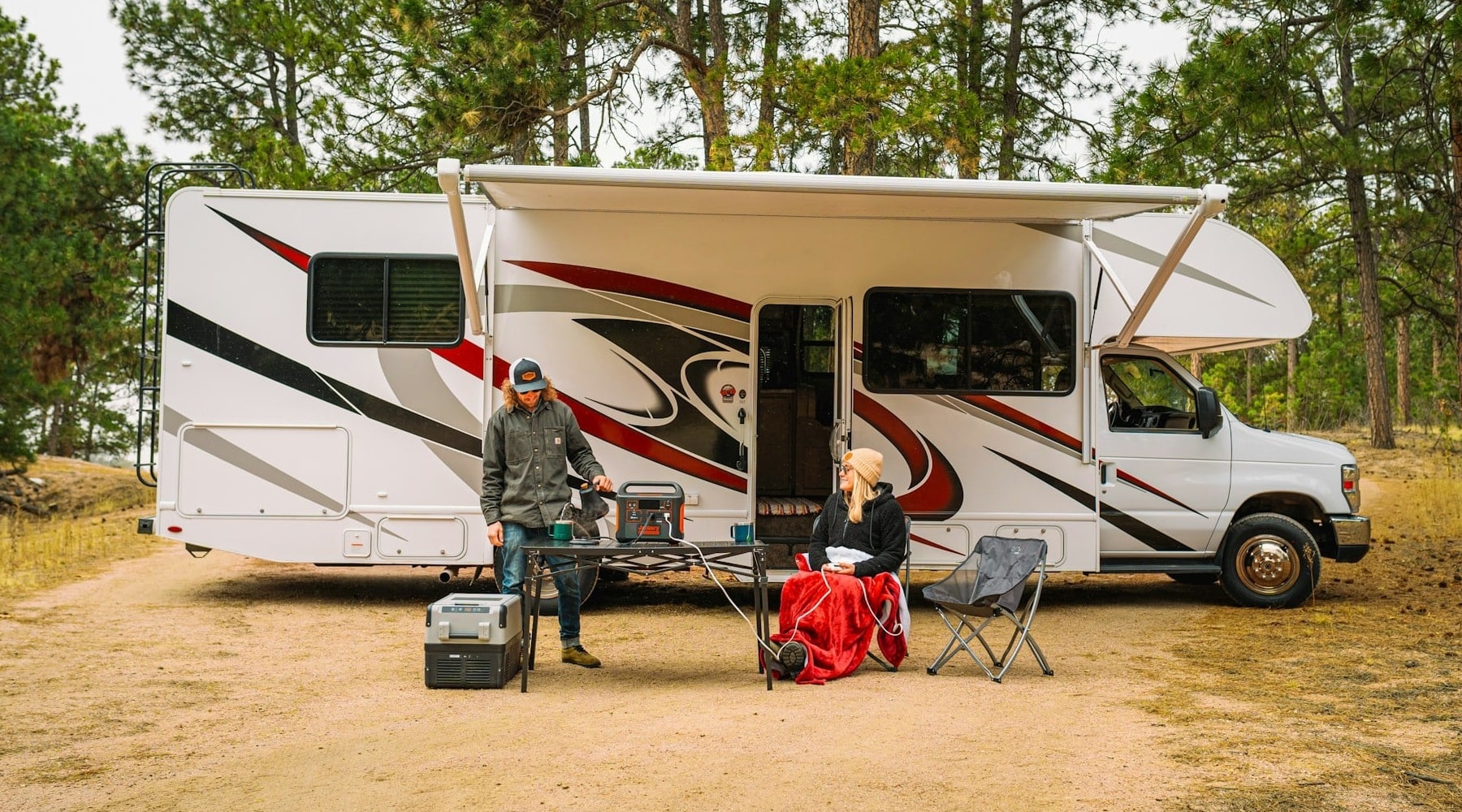 A photo of a man and a woman sitting outside their campervan with a portable power station.