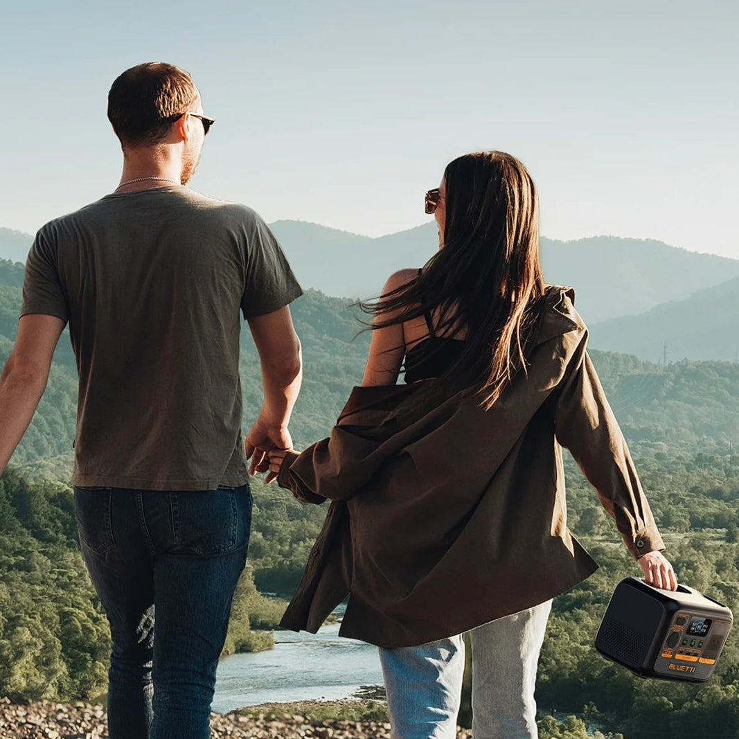 A picture showing a lady and a man outdoors holding hands whilst the lady also holds onto a bluetti AC2P 300w portable power station in her other hand.
