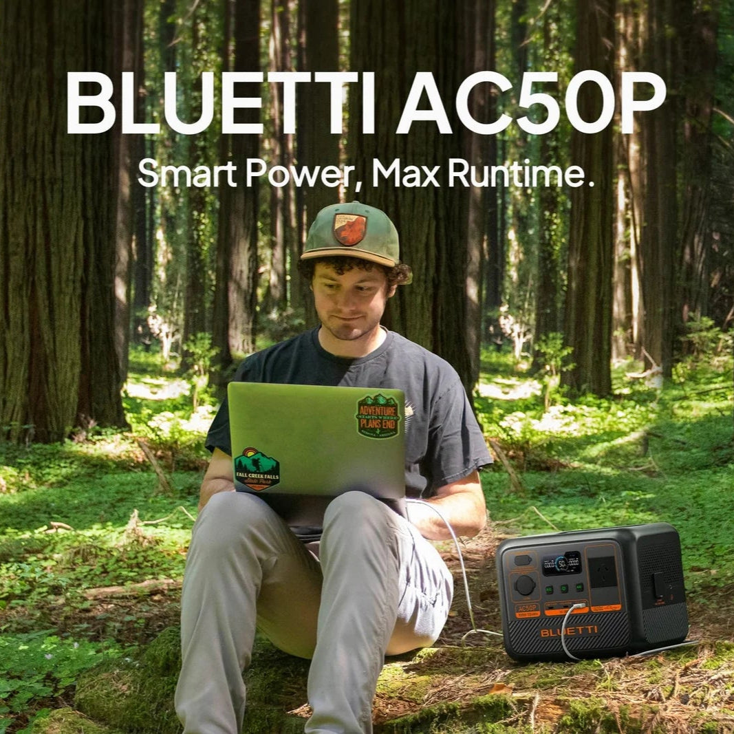 A photo of a man sitting out in the forest next to a Bluetti AC50P 700W portable power station charging his laptop.