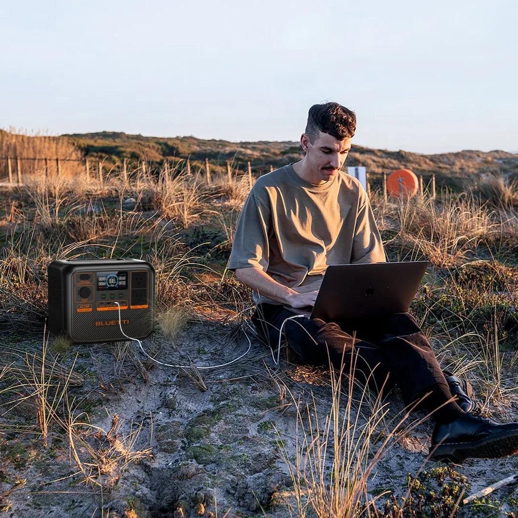 A picture of a man on a laptop sitting next to a bluetti ac70p 1000 portable power station in the outback.