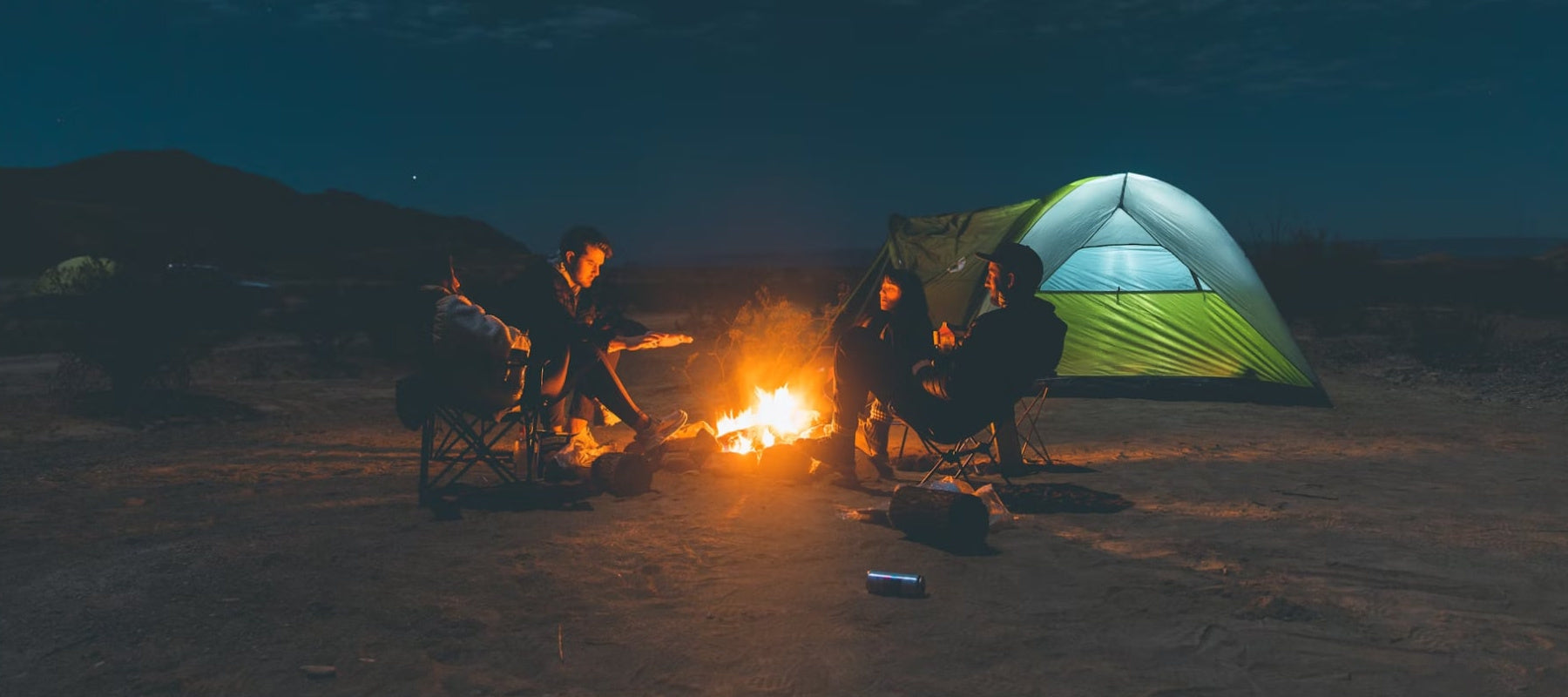 A photo of 4 people sitting outside near a campfire - Credit Caleb Fisher.