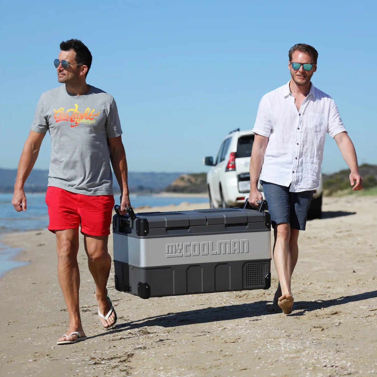 A photo of a MyCOOLMAN 85L Dual Zone Portable Car and Camping Fridge being carried by two men.