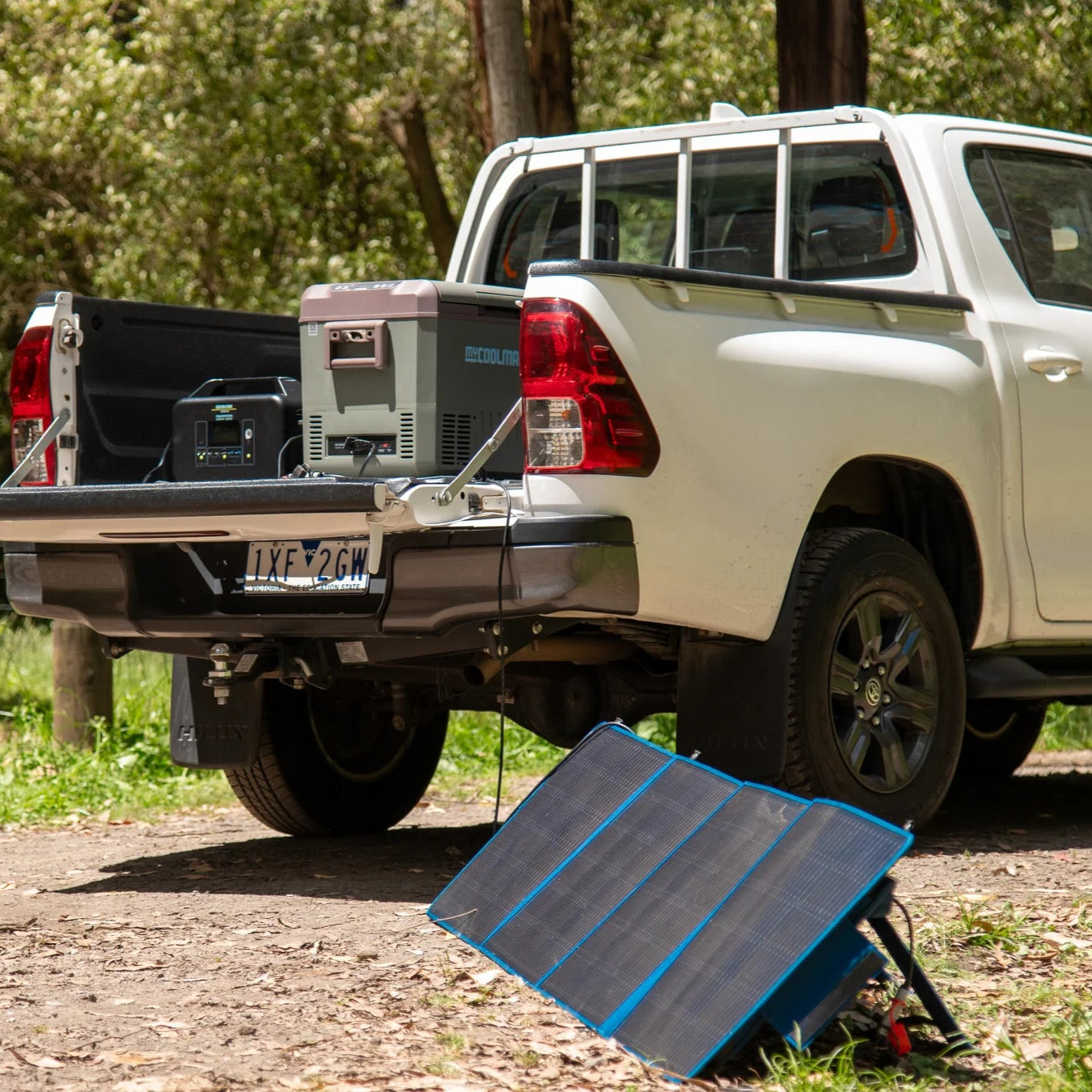 A photo of a MyCOOLMAN 1000W 78Ah Portable Power Station in the back of a ute whilst receiving power from a mycoolman solar blanket and charging a mycoolman fridge.