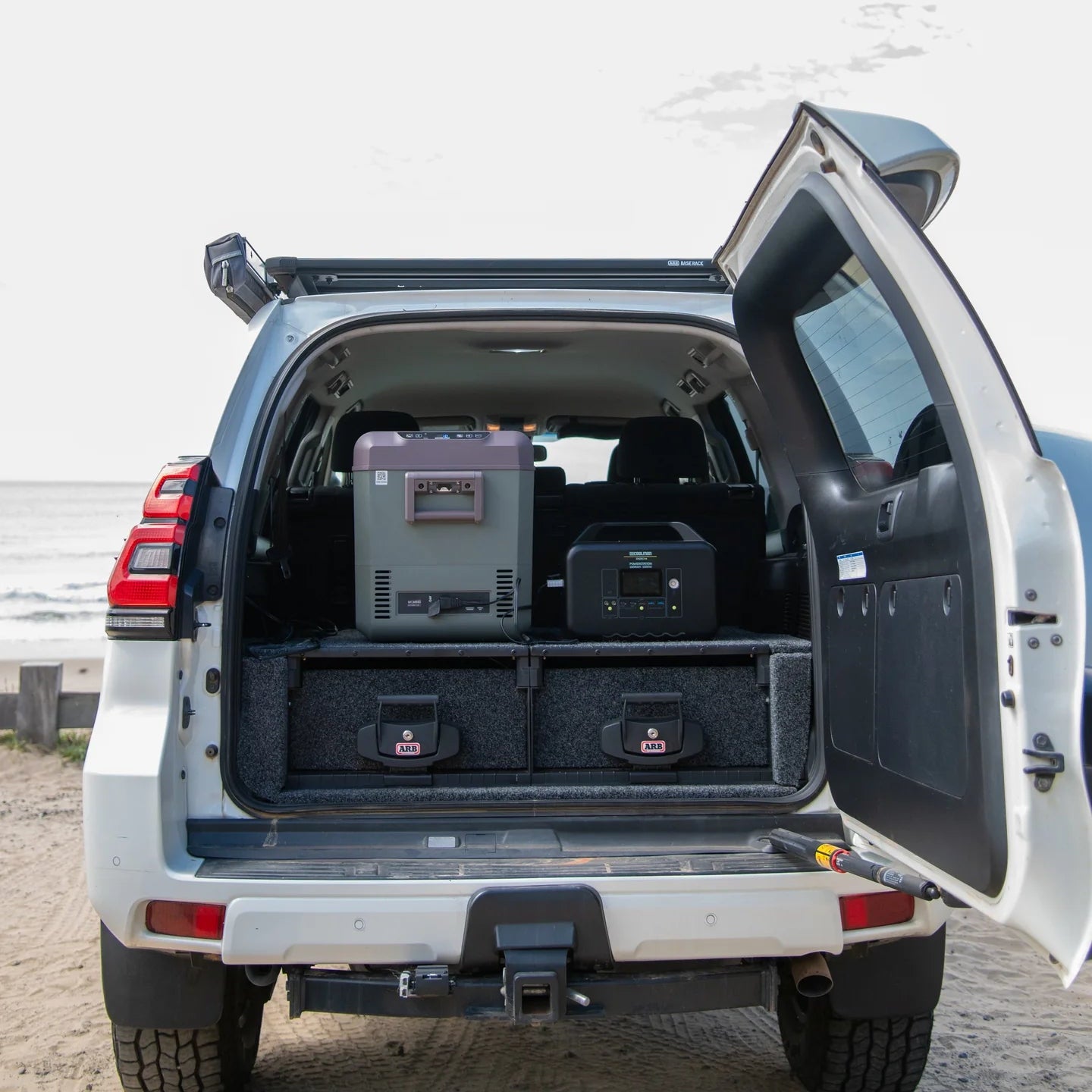 A photo of a MyCOOLMAN 1000W 78Ah Portable Power Station sitting in the back of a car next to a mycoolman fridge.