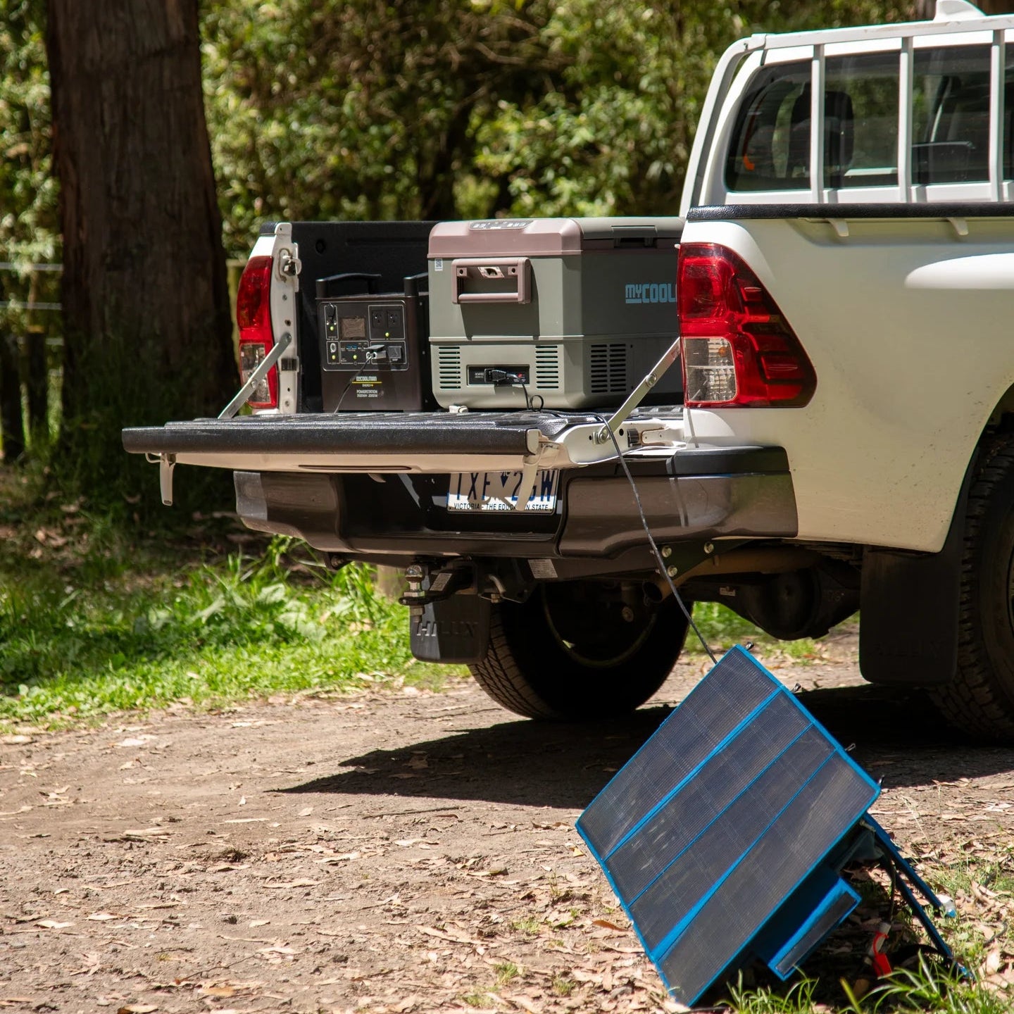 A photo of a mycoolman 2000W 150ah portable power station sitting in the back of a ute next to a mycoolman fridge and mycoolman solar blanket.