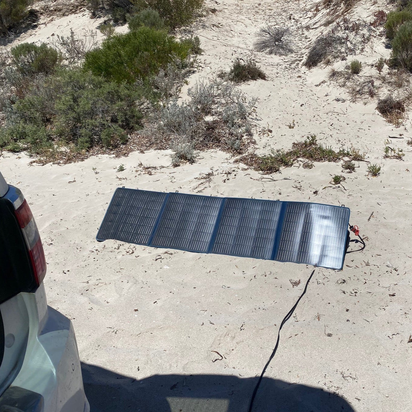 A photo of a MyCOOLMAN 200W flexible solar blanket on sand whilst plugged in.