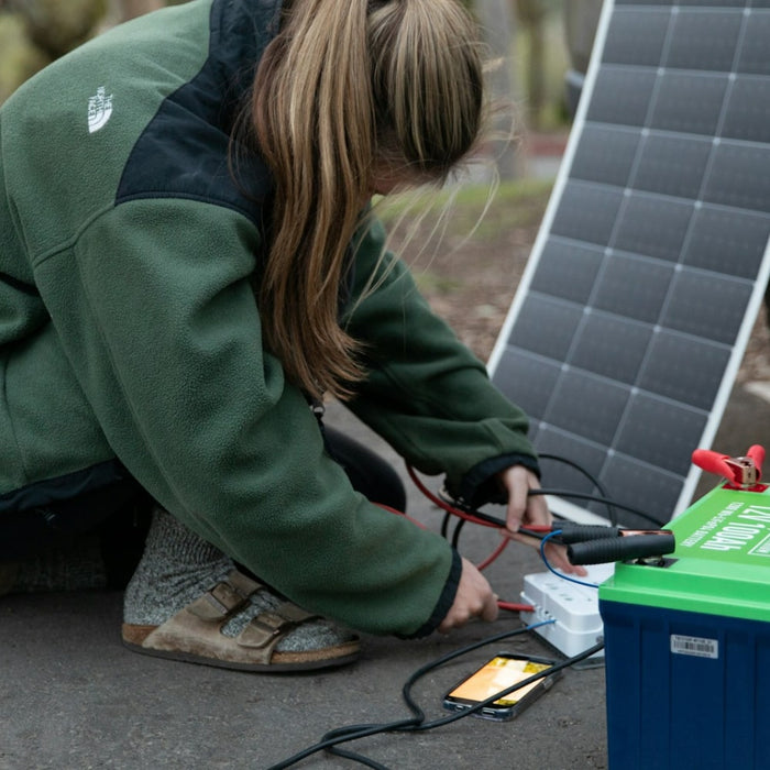 A picture showing a lady outdoors charging a solar panel via a battery
