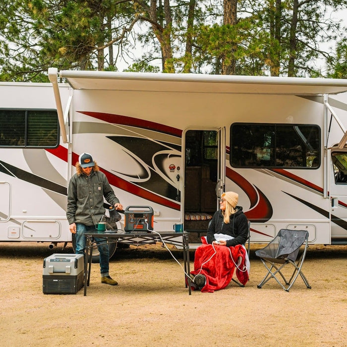 A photo of a man and a woman sitting outside their campervan with a portable power station.