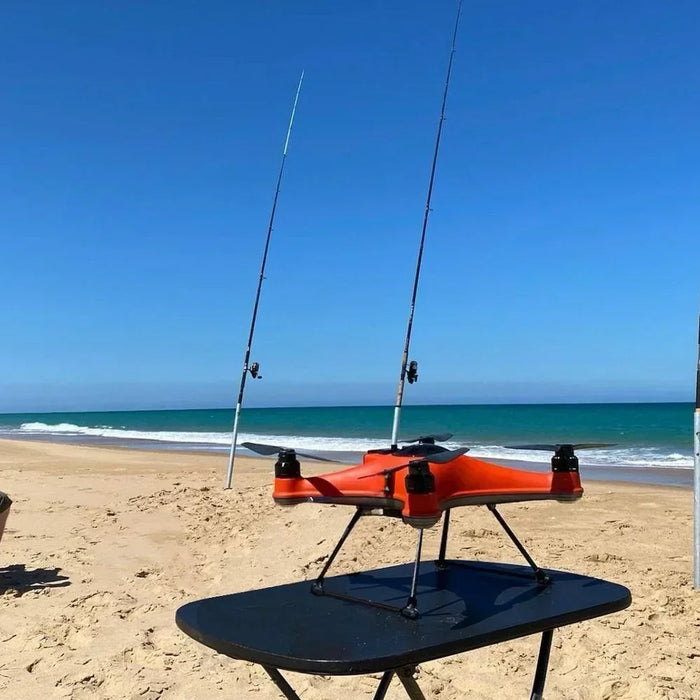A man sitting on a beach with fishing rods and a swellpro fishing drone.