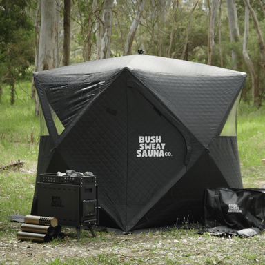 A photo of a 4-6 person portable sauna tent sitting next to a stove and accessories bag