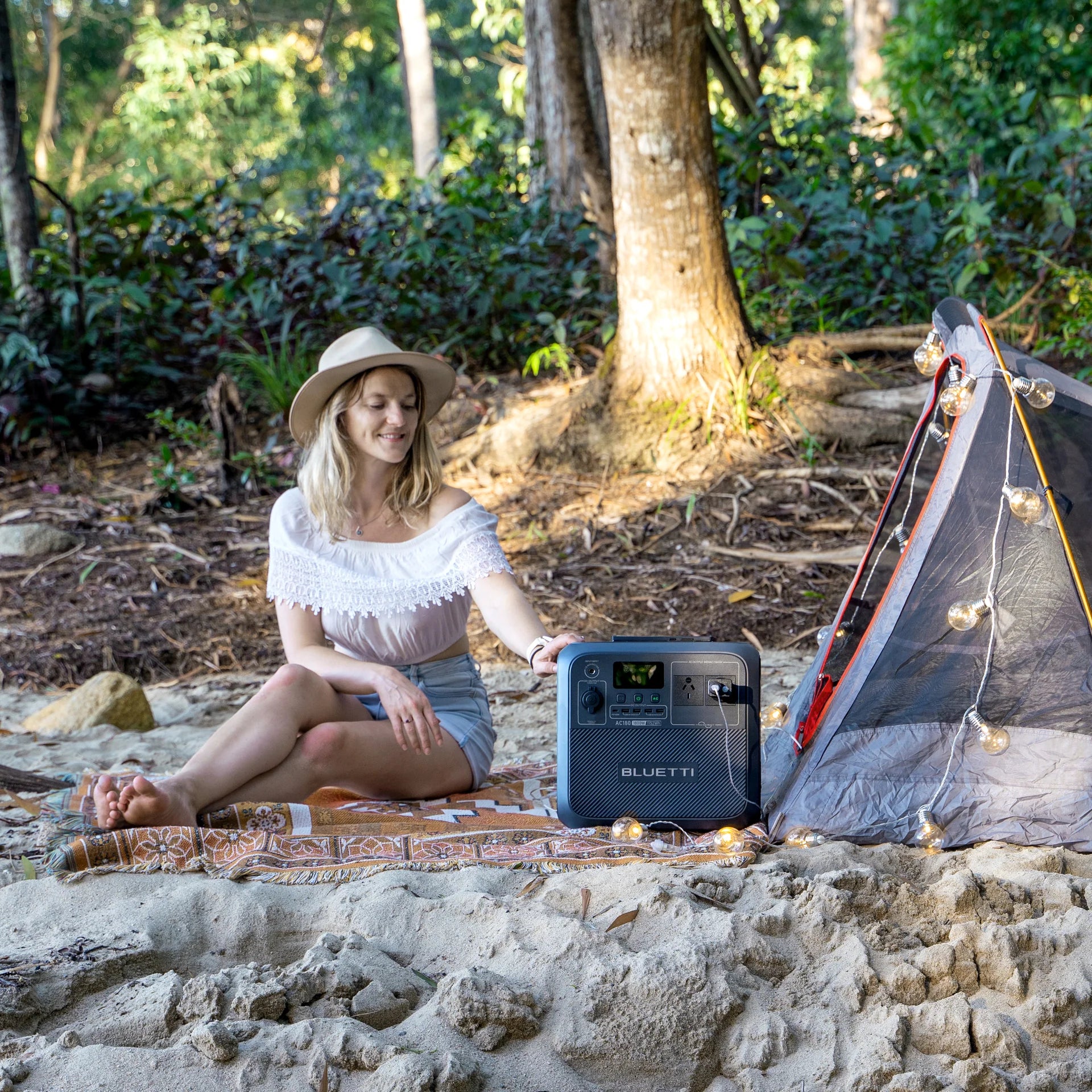 A photo of a lady in a campsite sitting next to a Bluetti AC180P Solar Portable power station.