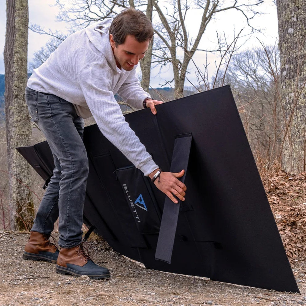 A photo of a man holding up a bluetti PV350 350W solar panel out in the bush.