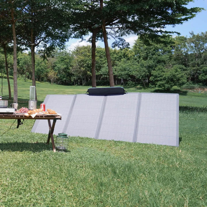 A photo of an EcoFlow 400W solar panel sitting on a bank of grass outdoors next to a table with food and appliances.