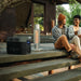 A photo of an EcoFlow Delta 2 Max Portable Power Station on a wooden deck, plugged into a light with two people sitting alongside.