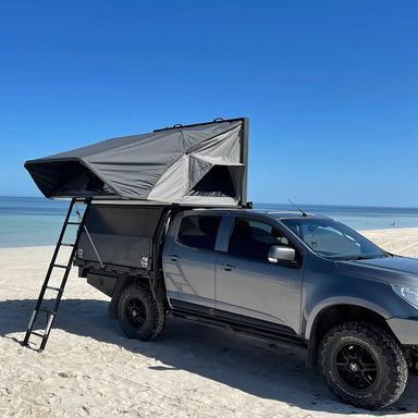 A photo of an Emroo desert king 4 person roof top tent sitting on top of a 4x4 on a beach with a ladder attached to the tent.