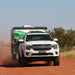 A Next Gen Ford Everest towing a camper trailer on a red dirt track in the Australian outback.
