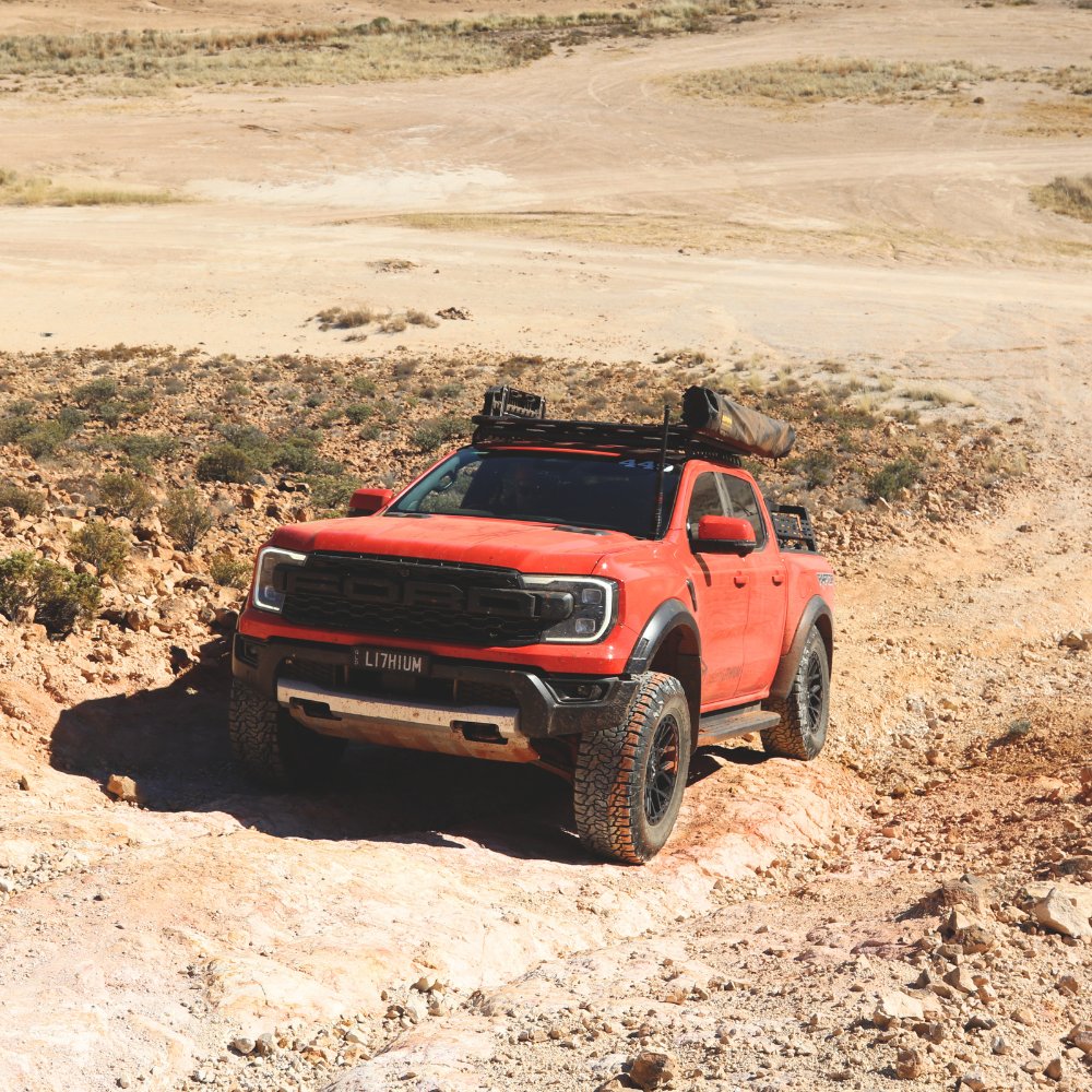 A Ford Ranger Raptor driving on a rocky off-road track in the Australian bush.