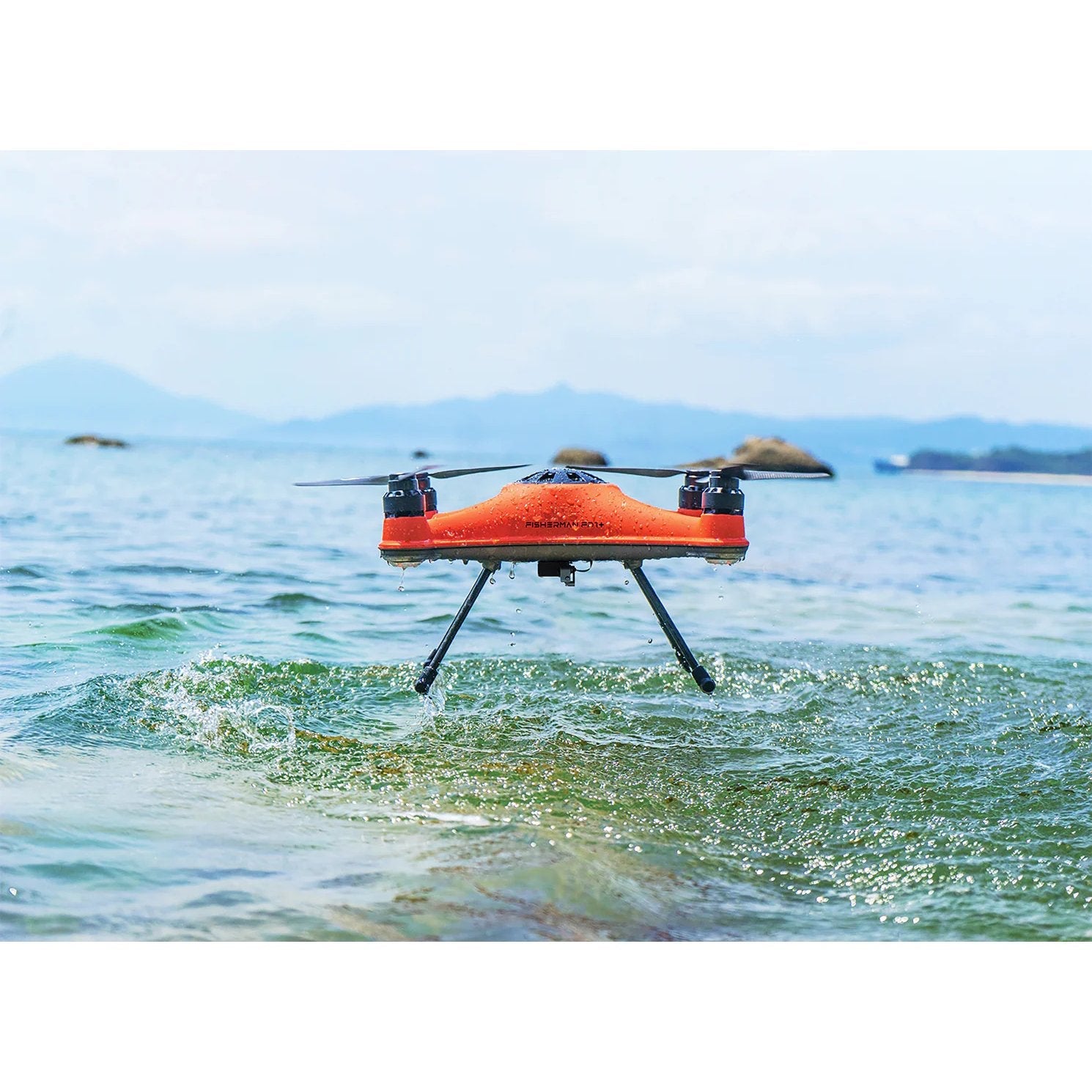 SwellPro Fisherman FD1S fishing drone lifting off the sea surface with water dripping from its landing gear and a rocky coastline behind.