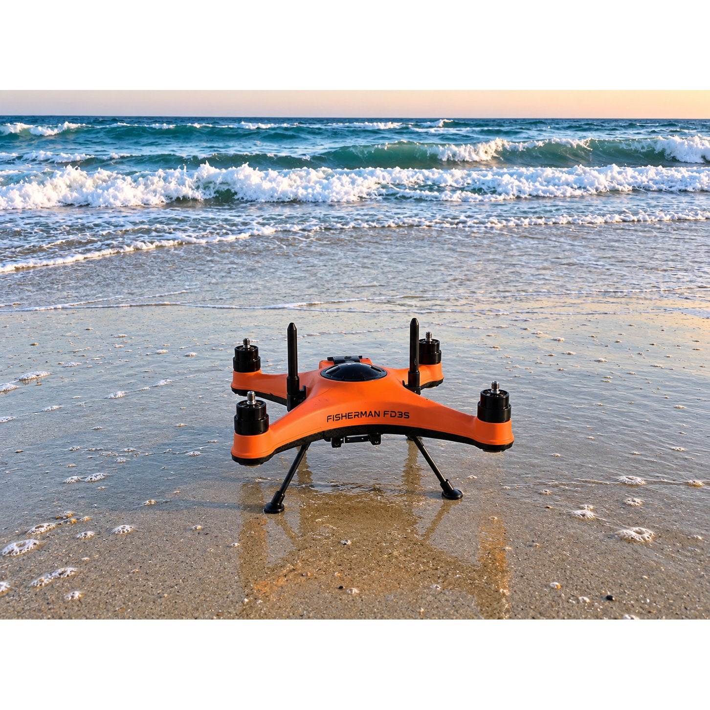 SwellPro Fisherman FD3S fishing drone standing on wet sand at the water's edge at sunset, with surf breaking behind it.